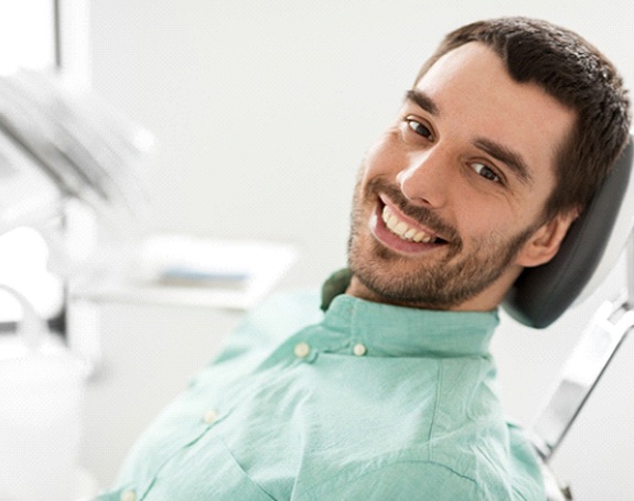 Man with veneers in dentist’s chair smiling