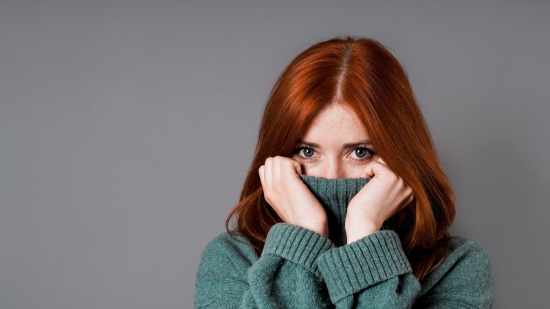 Woman hiding her smile with both hands pulling up her turtleneck